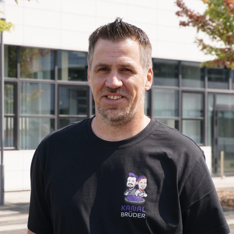 Mann mit kurzem Haar und freundlichem Lächeln in hellgrauem Pullover.