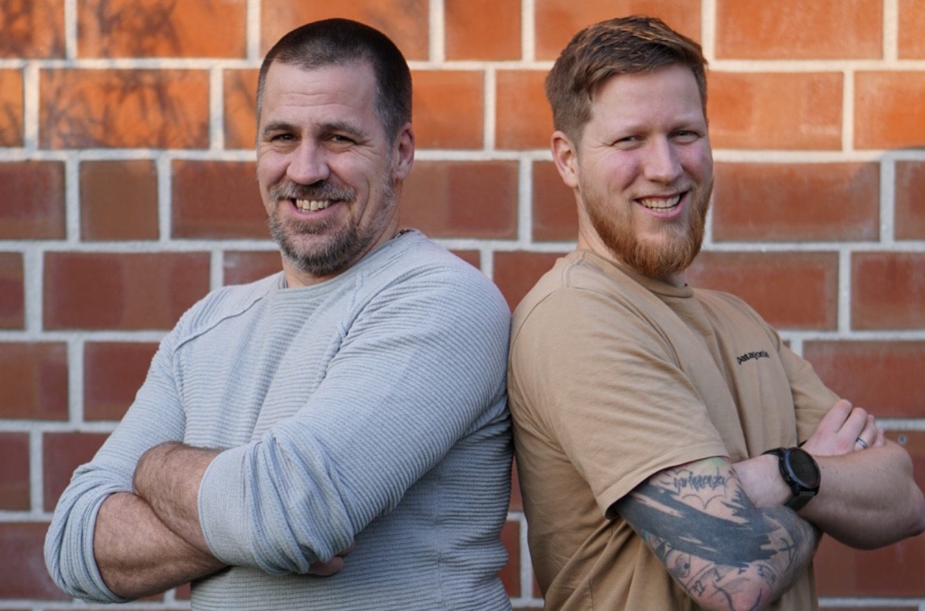 Timo und Pascal Elbers (Kanalbrüder) stehen Rücken an Rücken, lächeln und tragen lässige Kleidung.